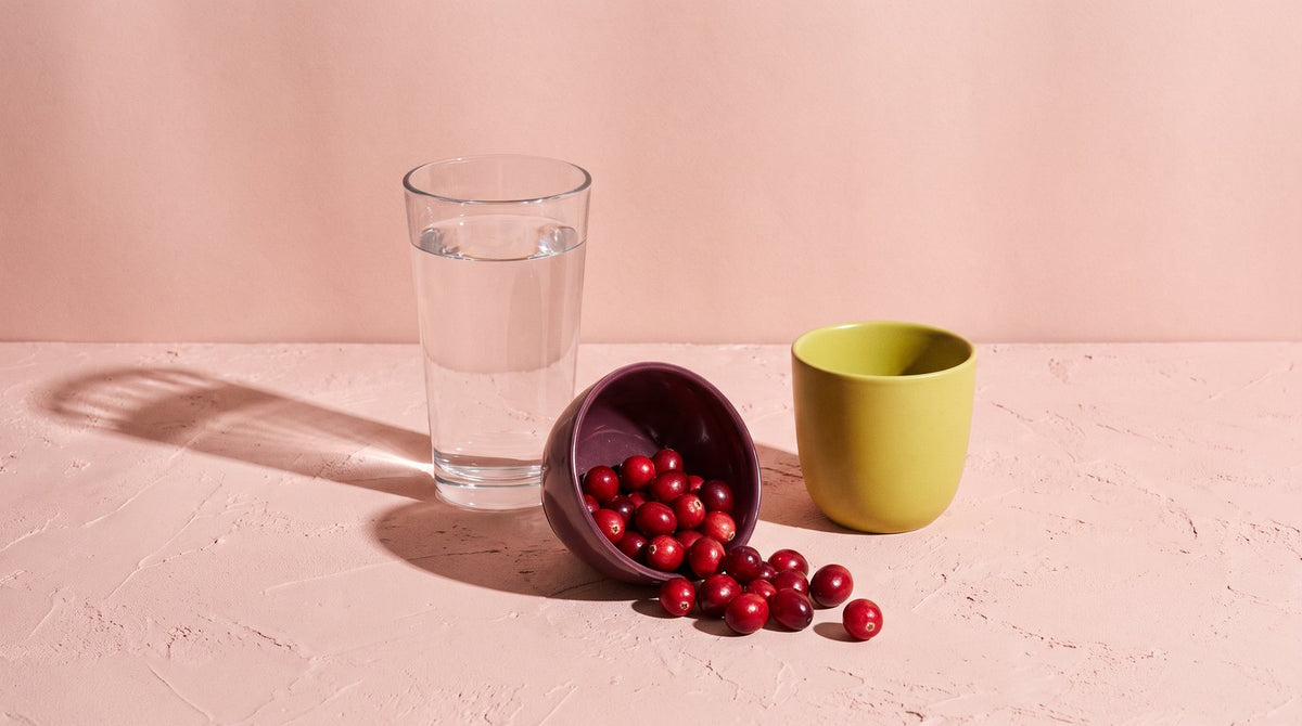 A glass of water, a tipped plum bowl of cranberries and a yellow-green cup on blush plaster