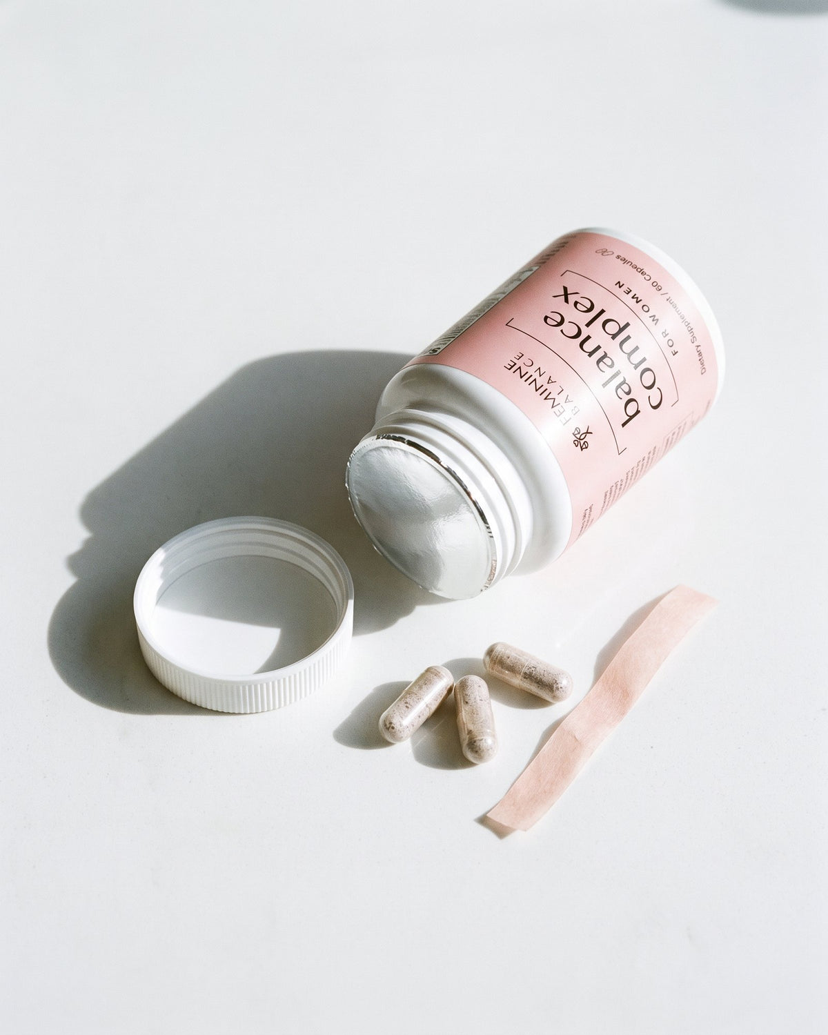 The open bottle with its cap set beside it and two capsules on a clean white counter