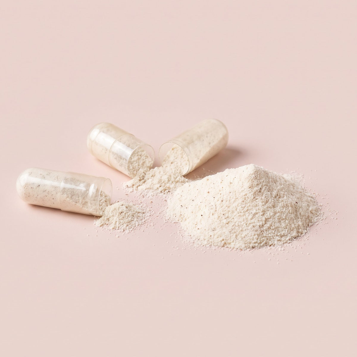 Three opened capsules spilling creamy probiotic powder beside a small mound of the powder on a blush surface