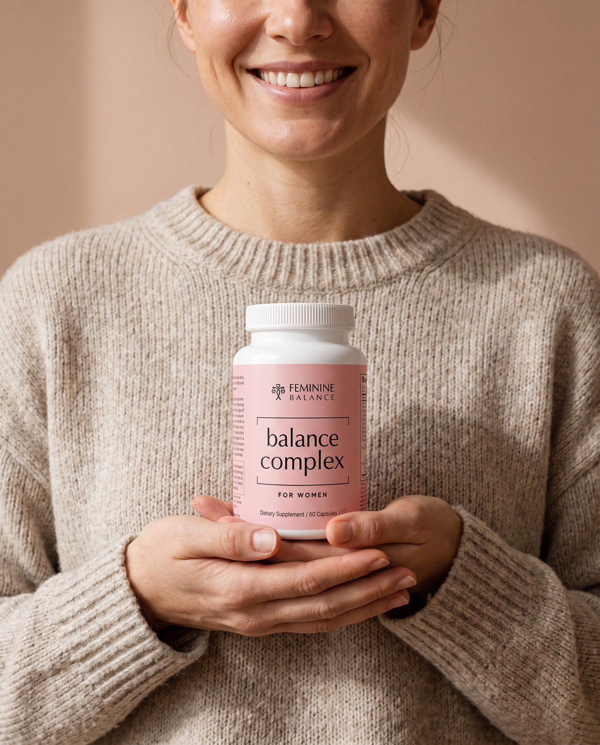 Nose-crop portrait: a smiling woman in an oatmeal knit cradling the Balance Complex bottle in both hands