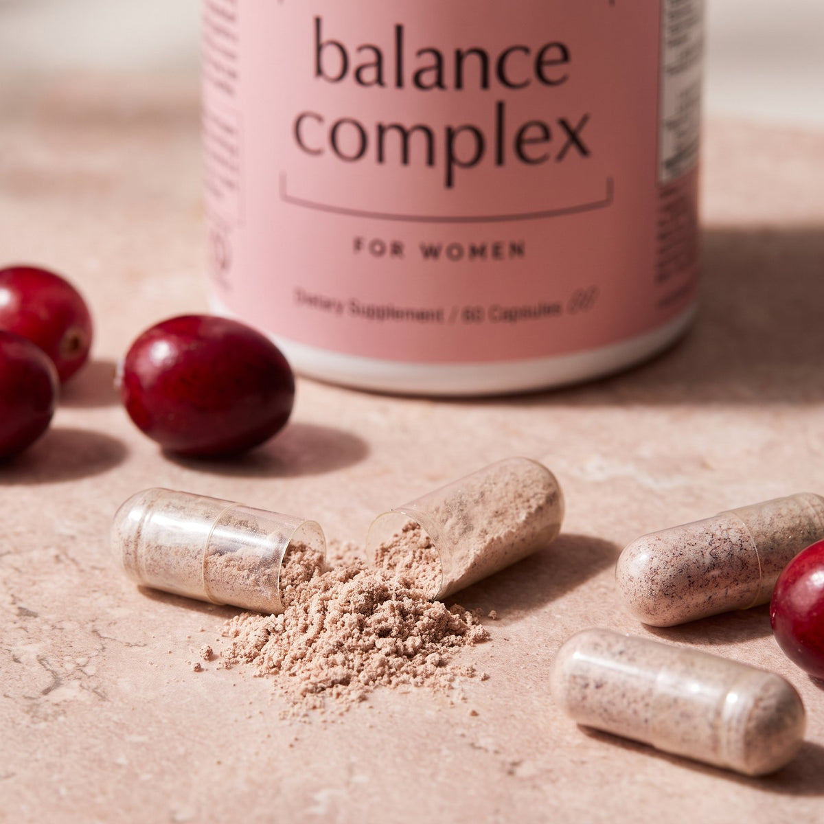 Close-up of an opened capsule spilling its powder beside fresh cranberries, the bottle behind