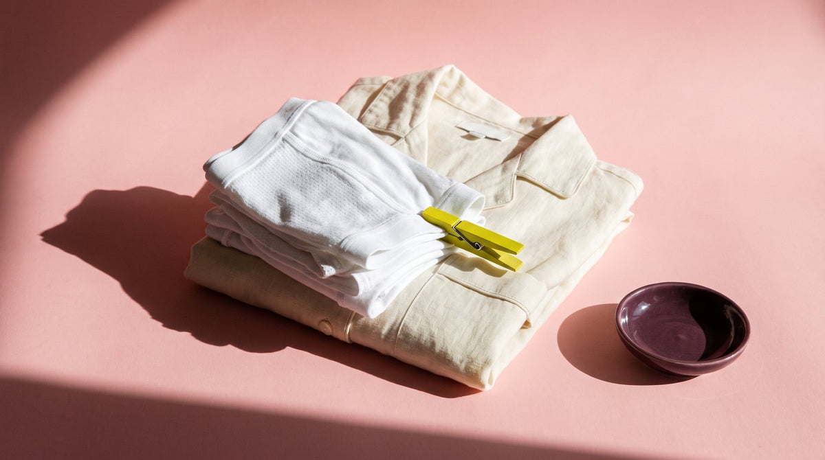 Folded white cotton underwear and loose linen sleepwear held with a yellow-green peg on blush